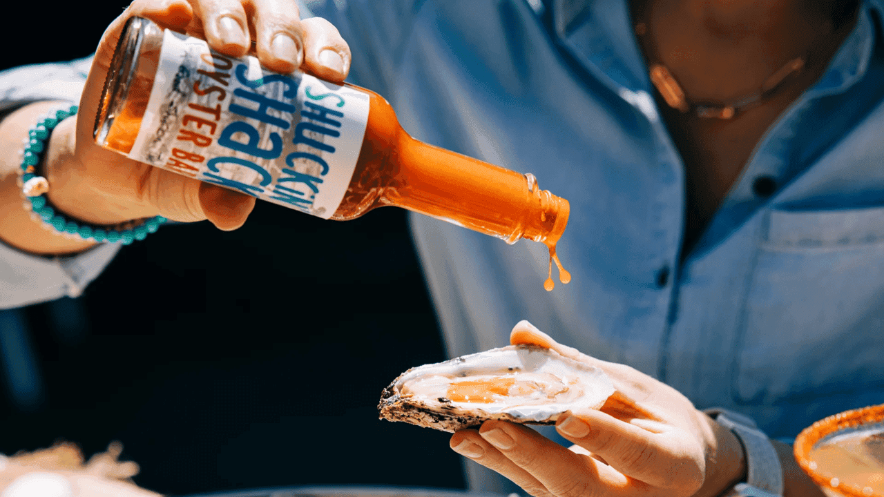 How undefined Evolved and Set New Standards Photo of person holding oyster and Shuckin' Shack hot sauce bottle