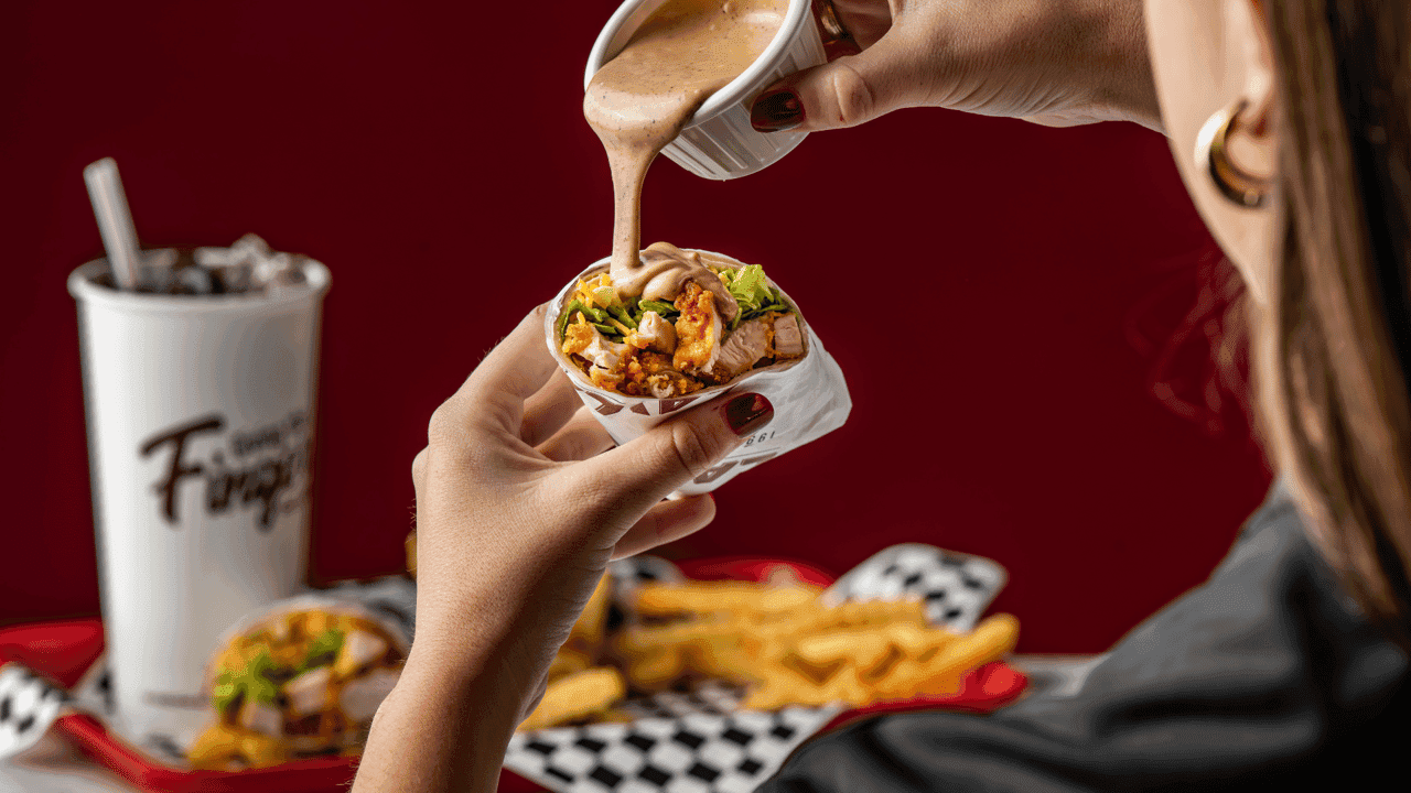 How undefined Evolved and Set New Standards Photo of person holding Layne's Chicken Fingers wrap, pouring sauce