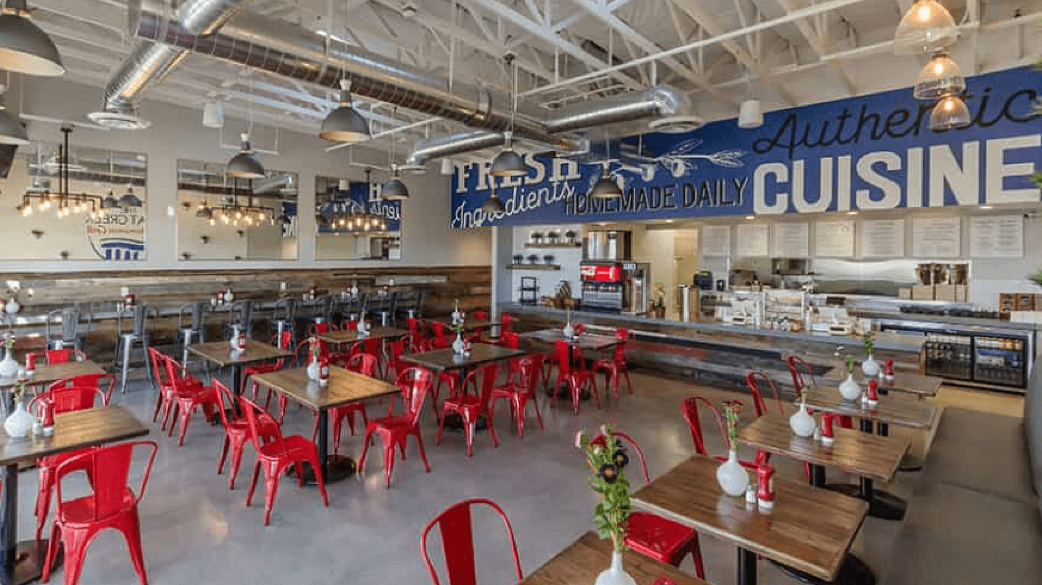 Interior of The Great Greek Grill with red chairs, wooden tables, and open kitchen setup